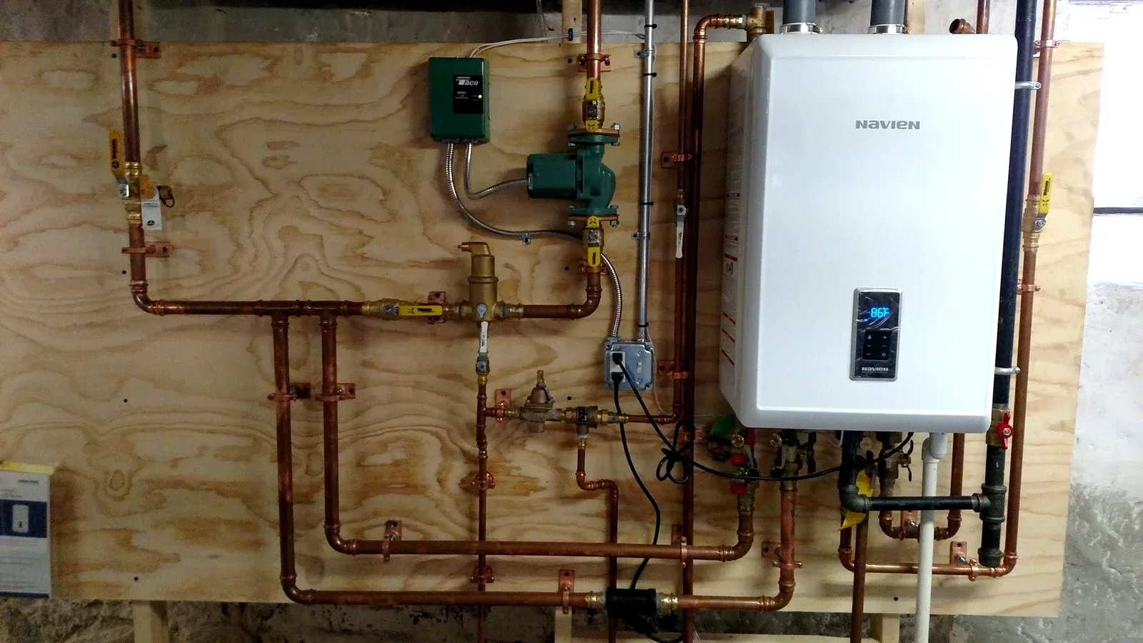 Navien tankless water heater installed by Prime Plumbing with a custom copper manifold on a mounting board in a Greater Boston basement